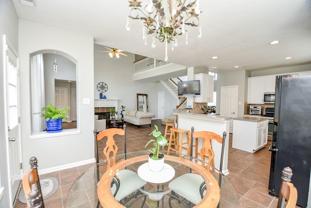 dining room featuring arched walkways, recessed lighting, a ceiling fan, stairway, and a tiled fireplace