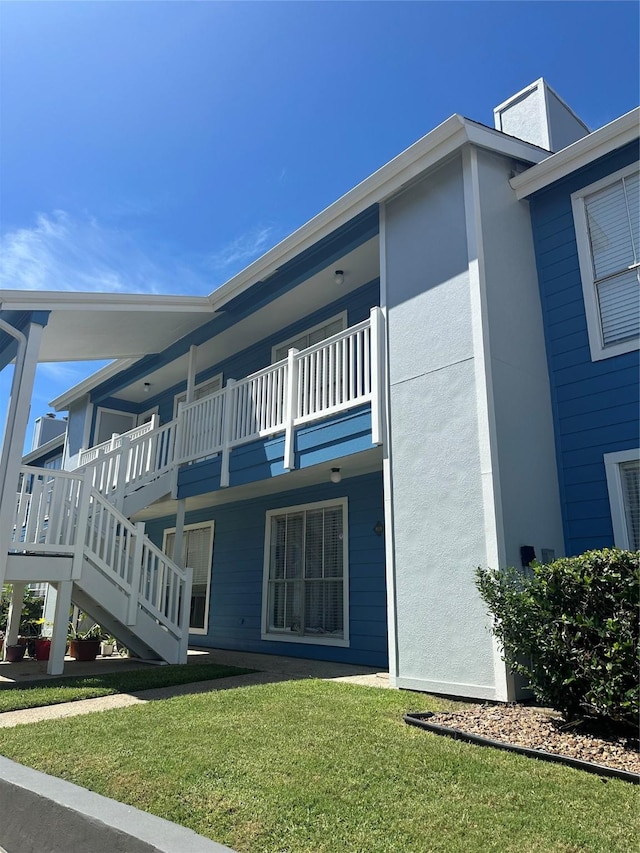 exterior space with a balcony, stucco siding, stairs, and a yard