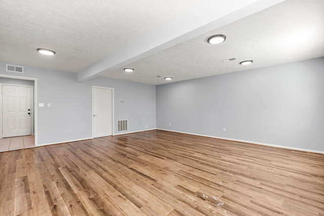 empty room with beamed ceiling, a textured ceiling, and light hardwood / wood-style flooring