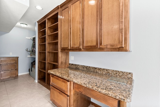 interior space with light tile patterned floors, stone countertops, baseboards, open shelves, and brown cabinetry