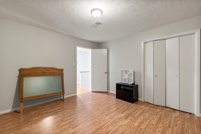 unfurnished bedroom with a textured ceiling, light wood-type flooring, and a closet