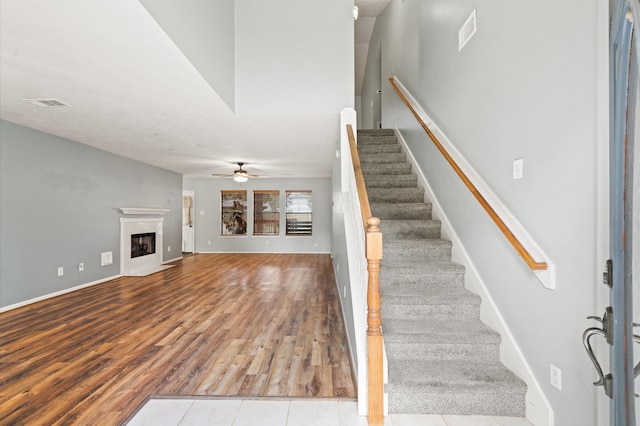 staircase featuring ceiling fan, hardwood / wood-style floors, and a high end fireplace