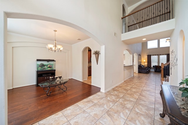 foyer featuring light wood-type flooring, a notable chandelier, crown molding, and a high ceiling