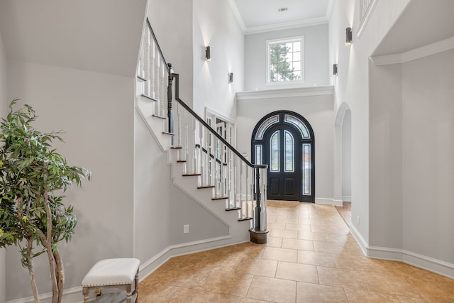 entrance foyer with a towering ceiling, light tile patterned floors, and crown molding