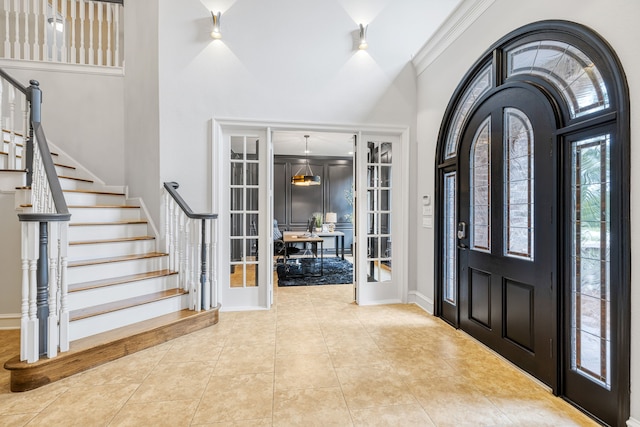 foyer entrance featuring a high ceiling, ornamental molding, light tile patterned floors, and french doors