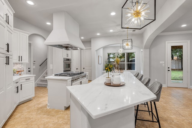 kitchen with custom range hood, hanging light fixtures, white cabinets, stainless steel appliances, and a kitchen island with sink