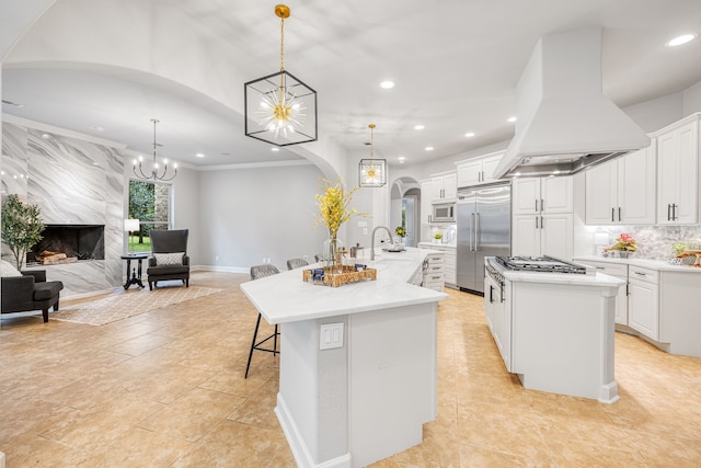 kitchen featuring white cabinets, a high end fireplace, built in appliances, custom range hood, and a spacious island