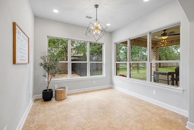 unfurnished sunroom featuring ceiling fan with notable chandelier and a wealth of natural light