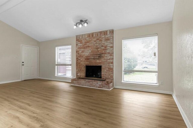 unfurnished living room with hardwood / wood-style flooring, vaulted ceiling, plenty of natural light, and a brick fireplace