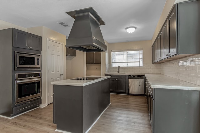 kitchen featuring decorative backsplash, appliances with stainless steel finishes, light hardwood / wood-style floors, and custom range hood