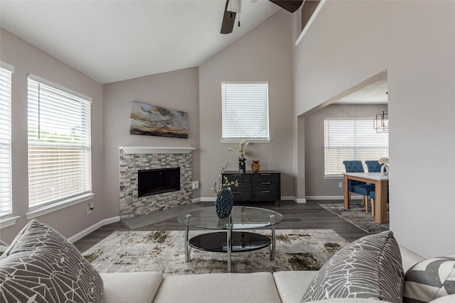 living room with ceiling fan, a stone fireplace, vaulted ceiling, and dark wood-type flooring