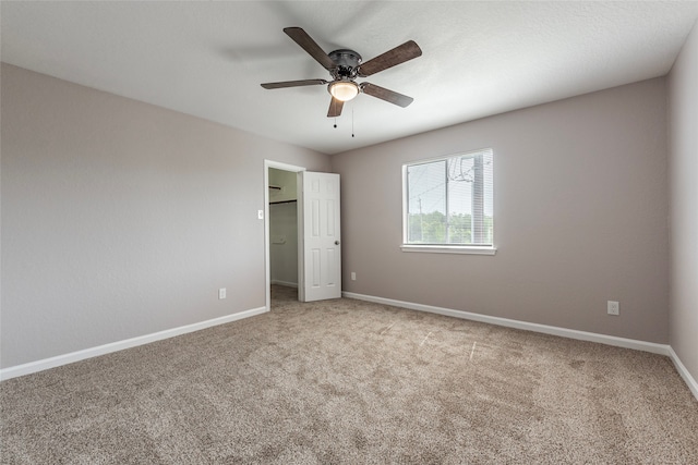 unfurnished bedroom with a spacious closet, a closet, ceiling fan, and light carpet