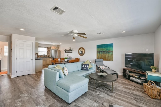 living room with a textured ceiling, ceiling fan, wood finished floors, visible vents, and baseboards