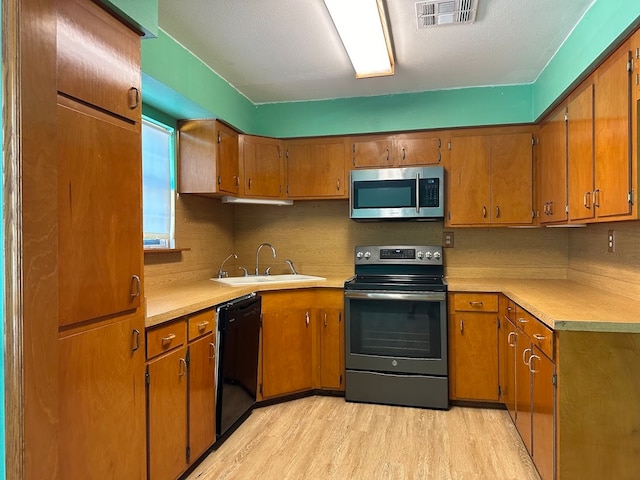 kitchen with sink, stainless steel appliances, light hardwood / wood-style floors, and a textured ceiling