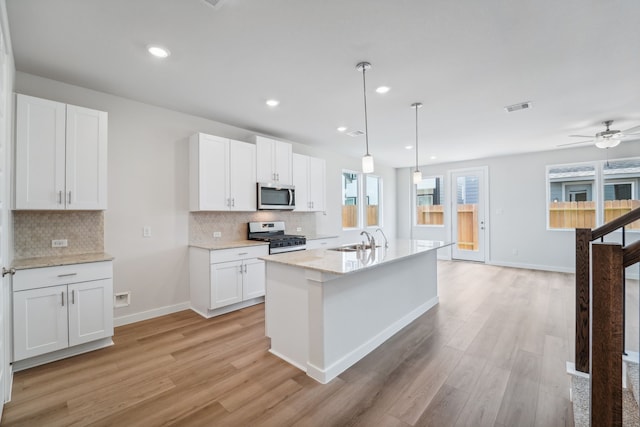 kitchen with white gas range oven, pendant lighting, a center island with sink, white cabinets, and light wood-type flooring