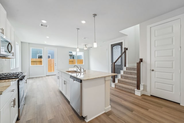 kitchen with a kitchen island with sink, white cabinets, pendant lighting, and appliances with stainless steel finishes