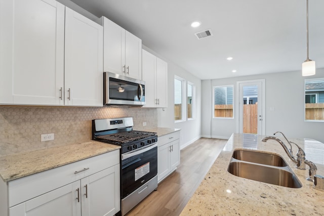 kitchen with sink, hanging light fixtures, stainless steel appliances, light stone counters, and white cabinets