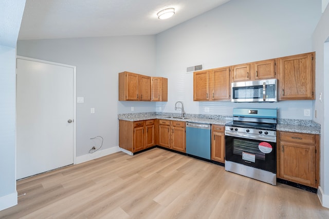 kitchen with appliances with stainless steel finishes, sink, light stone counters, light wood-type flooring, and high vaulted ceiling