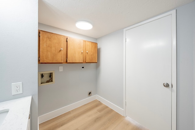 washroom with a textured ceiling, light hardwood / wood-style flooring, electric dryer hookup, and cabinets