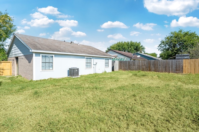 rear view of property with central AC unit and a yard