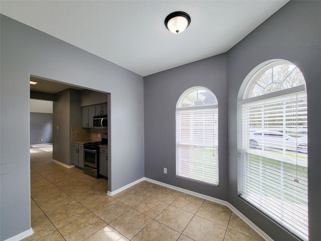 empty room featuring a textured ceiling, light tile patterned floors, and a wealth of natural light