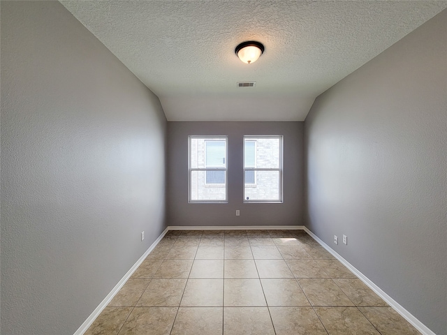 tiled empty room with a textured ceiling and vaulted ceiling