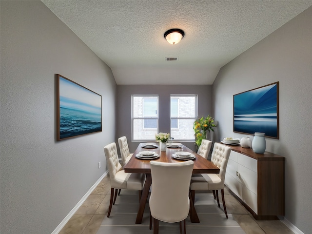 tiled dining room featuring a textured ceiling and lofted ceiling