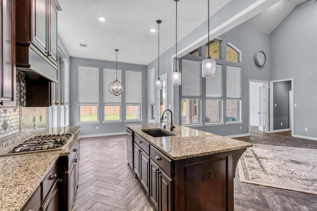 kitchen with light stone countertops, dark brown cabinets, stainless steel appliances, sink, and an island with sink