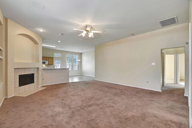 unfurnished living room with a tile fireplace, ceiling fan, and light colored carpet