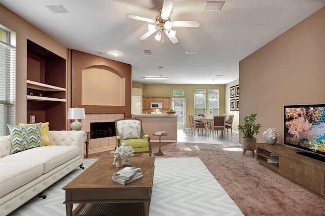 carpeted living room featuring ceiling fan and a tiled fireplace