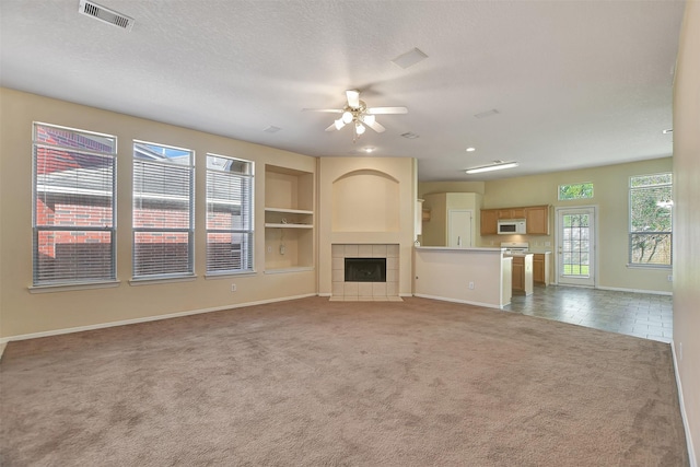 unfurnished living room featuring built in shelves, ceiling fan, a tile fireplace, a textured ceiling, and carpet