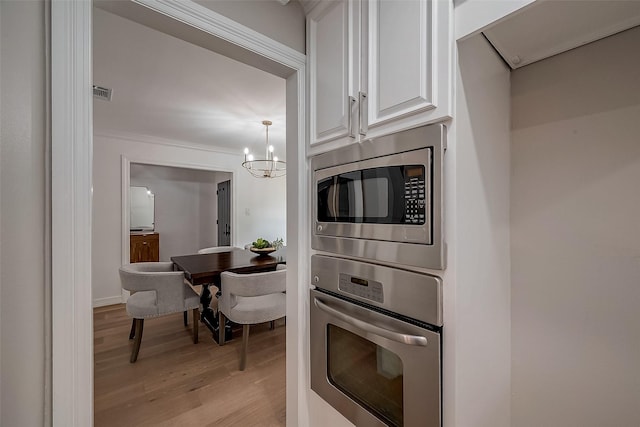 kitchen with hanging light fixtures, stainless steel appliances, light hardwood / wood-style flooring, a notable chandelier, and white cabinets