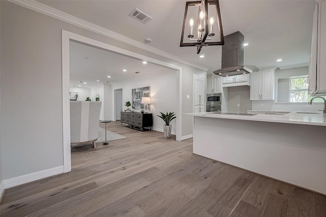 kitchen with stainless steel microwave, sink, gas cooktop, island exhaust hood, and white cabinets