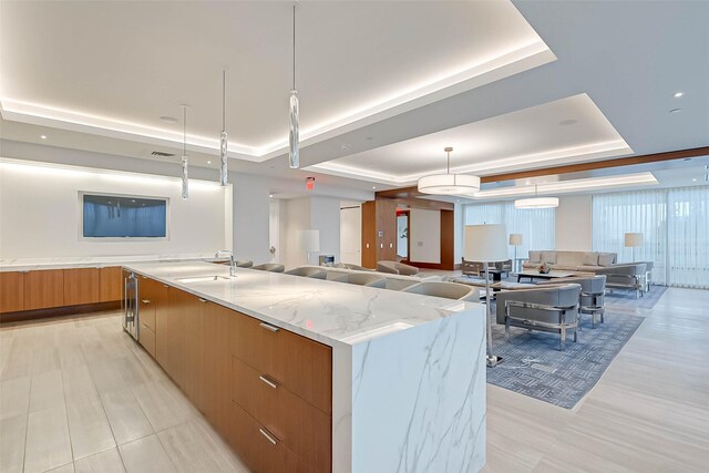 kitchen with hanging light fixtures, a large island, a tray ceiling, and light stone countertops