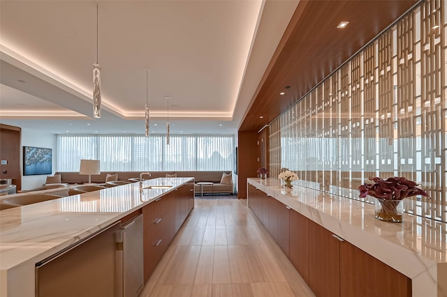 kitchen featuring sink, a spacious island, light stone counters, light tile patterned floors, and a raised ceiling