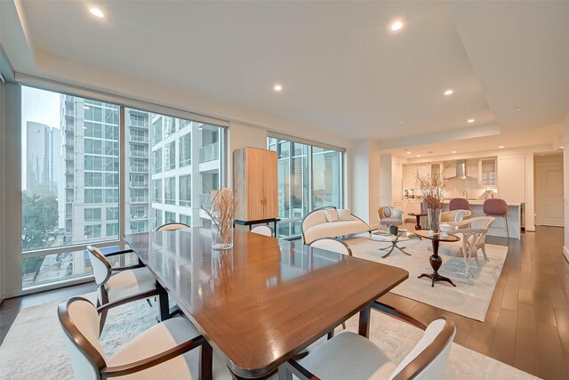 dining area featuring hardwood / wood-style flooring, a raised ceiling, and a wall of windows