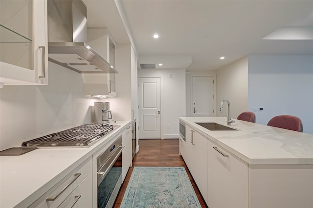 kitchen featuring appliances with stainless steel finishes, white cabinetry, sink, wall chimney range hood, and dark hardwood / wood-style flooring