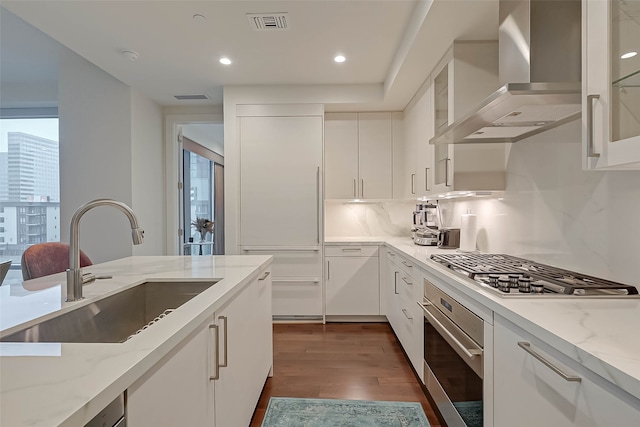 kitchen with sink, appliances with stainless steel finishes, wall chimney exhaust hood, dark hardwood / wood-style floors, and a healthy amount of sunlight