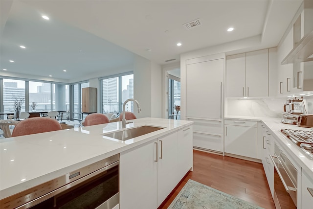 kitchen featuring stainless steel appliances, light hardwood / wood-style floors, decorative backsplash, sink, and white cabinets