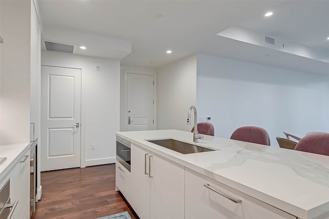 kitchen featuring sink, stainless steel microwave, light stone countertops, white cabinets, and dark hardwood / wood-style flooring