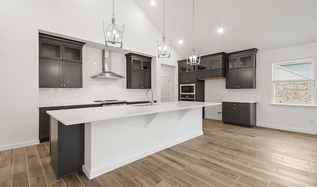 kitchen with sink, a kitchen island with sink, wall chimney range hood, and decorative backsplash