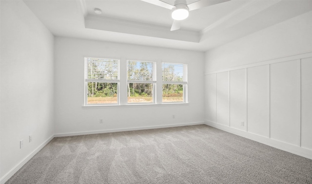 carpeted spare room with a raised ceiling and ceiling fan