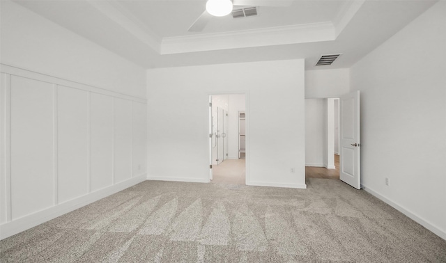 empty room with a raised ceiling, crown molding, and light colored carpet