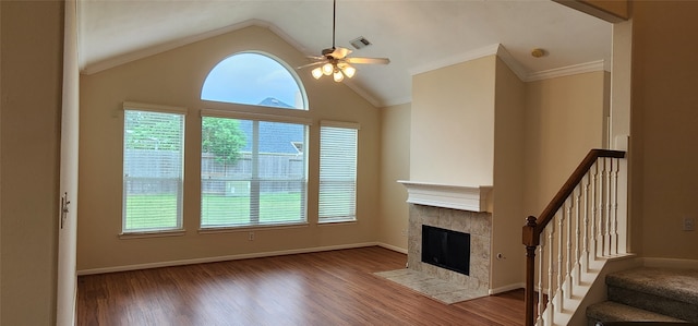 unfurnished living room with vaulted ceiling, dark hardwood / wood-style floors, a tiled fireplace, crown molding, and ceiling fan