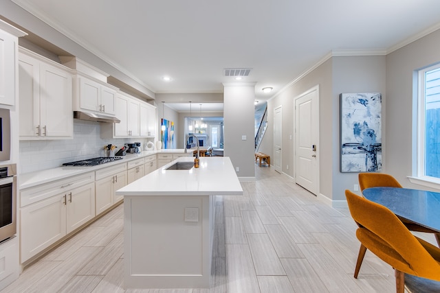 kitchen featuring tasteful backsplash, ornamental molding, white cabinets, appliances with stainless steel finishes, and sink