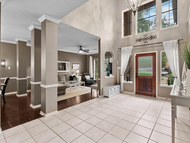 entrance foyer featuring light tile patterned flooring, ornamental molding, and ceiling fan with notable chandelier