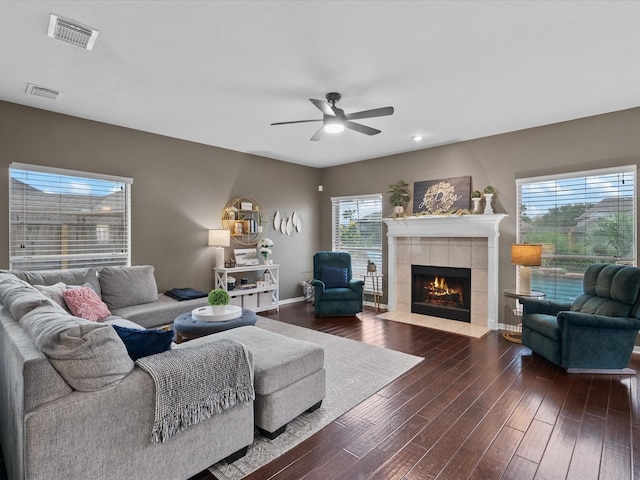 living room with dark hardwood / wood-style flooring, ceiling fan, a tile fireplace, and a healthy amount of sunlight