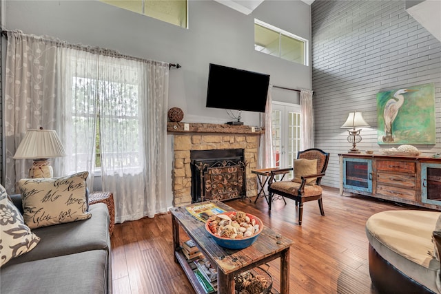 living room with a towering ceiling, a stone fireplace, and wood-type flooring