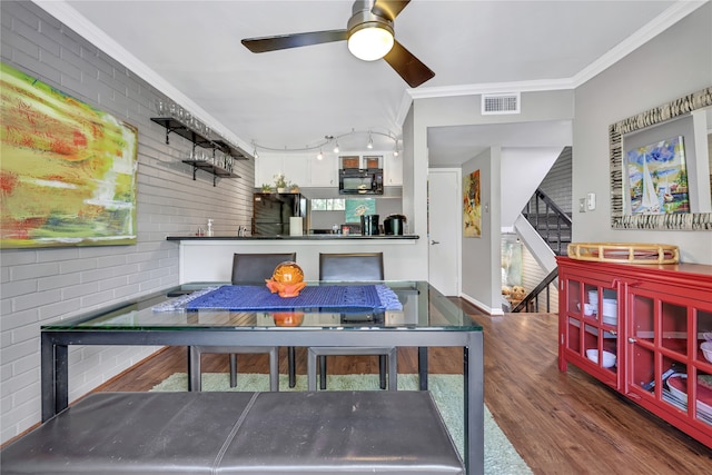 dining room with rail lighting, dark wood-type flooring, ceiling fan, crown molding, and brick wall