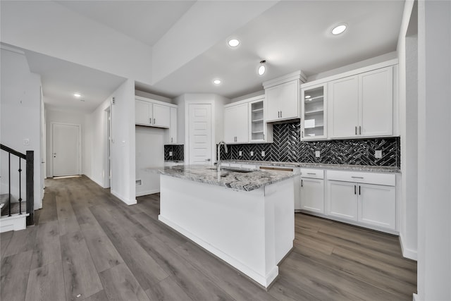 kitchen with white cabinets, light hardwood / wood-style floors, a center island with sink, and light stone counters